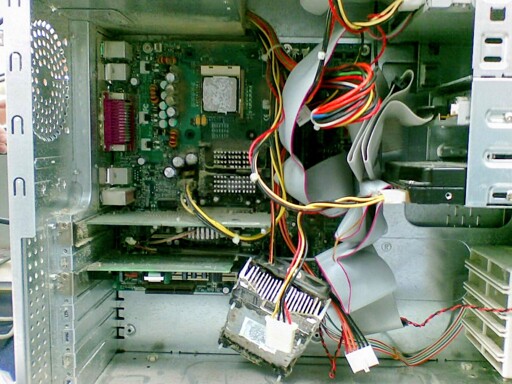 Inside a computer case showing a green motherboard with CPU socket, various colored cables (red, yellow, black), a hard drive, and metal casing components. The cooler has fallen off the CPU.